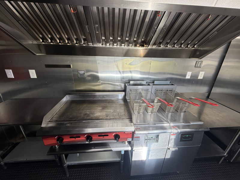 Food trailer interior showing fryers, flattop grill and prep area