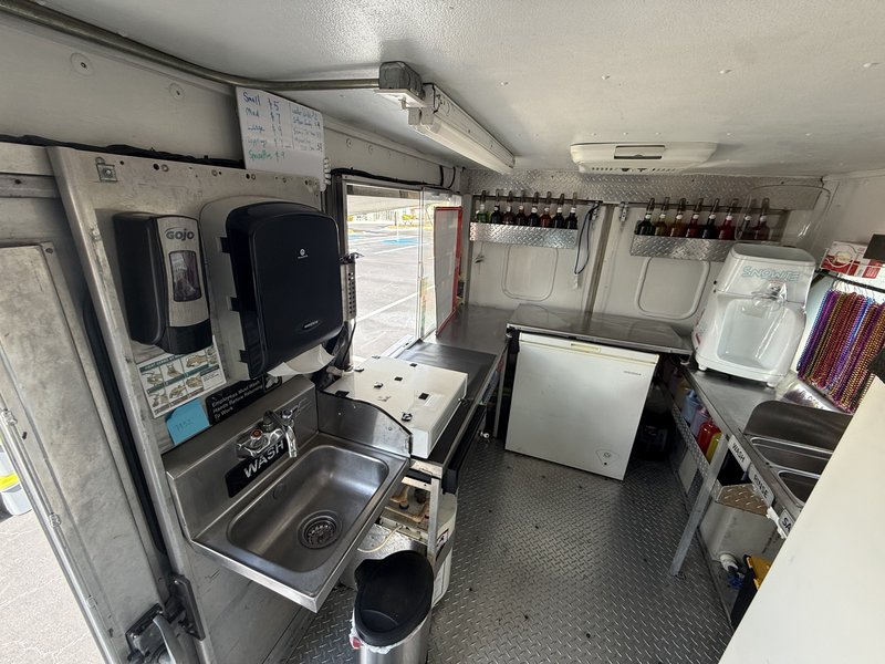 Interior galley of a turnkey shaved ice truck for sale in Florida — hand-wash sink, syrup pump rack, freezer, and diamond-plate walls