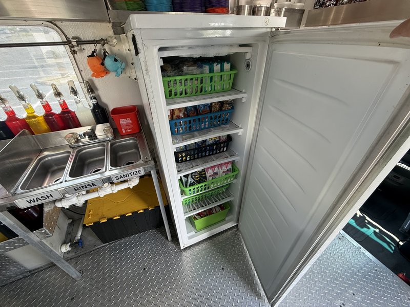 Upright commercial freezer with stocked storage baskets inside a frozen treats food truck for sale in Florida
