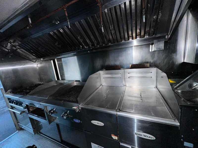 Kitchen Area of Food Truck For Sale with Hood and Suppression Cooking line with range, griddle, grill, twin fryers and exhaust hood